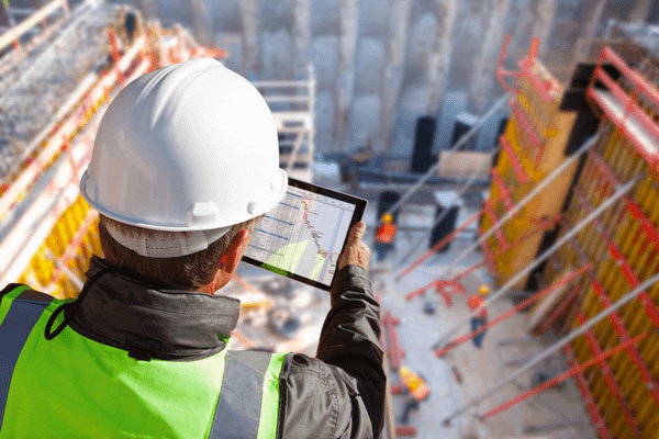 Construction worker overlooking construction site wile looking at a tablet